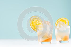 Homemade oranges cold drink with orange liquor, ice cubes in misted shot glass on soft light pastel blue background.