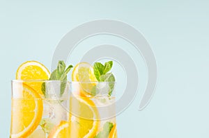 Homemade oranges lemonades with slices, ice cubes, mint in wet wineglasses on blue background,  closeup, top section, edge.