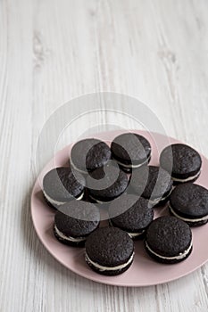 Homemade Oreos on a pink plate on a white wooden background, low angle view. Copy space