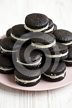 Homemade Oreos on a pink plate on a white wooden surface, low angle view