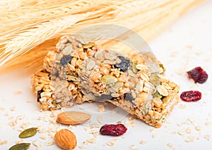 Homemade organic granola cereal bar with nuts and dried fruit on white background with oats and raw wheat.