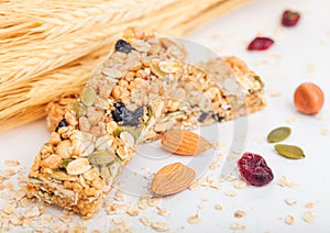 Homemade organic granola cereal bar with nuts and dried fruit on white background with oats and raw wheat.