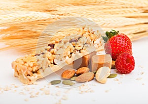 Homemade organic granola cereal bar with nuts and dried fruit on white background with oats and raw wheat. Strawberry and raspberr