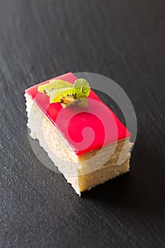 Homemade organic piece of vanilla sponge cake red berry sauce on black slate stone plate with copy space