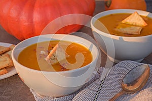 Homemade Organic Pumpkin Soup with Crackers and Pumpkin Seeds in White Bowls. Vegetarian Autumn soup.