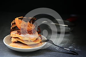 Homemade pancakes with orange candy top up and fork on dark background
