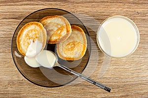 Homemade pancakes poured condensed milk, spoon in saucer, bowl with condensed milk on table. Top view