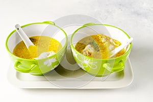 Homemade pasta chicken soup served in light green bowls with ceramic spoons on a white tray on white background