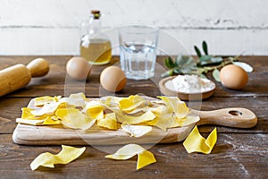 Homemade pasta Maltagliati on cutting board with ingredients on wooden background