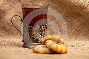 Homemade pastry cookies with jam and a faceted glass of tea in a vintage Cup holder on a background of homespun fabric with a