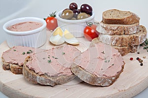 Homemade pate, olives, tomatoes and slices of bread on wooden board