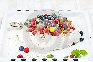 Homemade Pavlova cake with fresh garden and forest berries on white baking tray over light wooden background