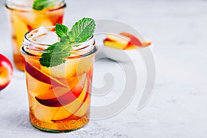 Homemade peach iced tea or lemonade with fresh mint and ice cubes in glass jar