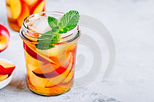 Homemade peach iced tea or lemonade with fresh mint and ice cubes in glass jar