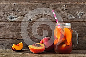 Homemade peach iced tea in a mason jar glass with cut fruit against rustic wood