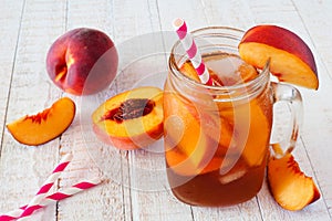 Homemade peach iced tea in a mason jar glass with a white wood background