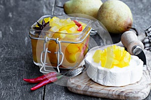 Homemade pear and chilli pepper chutney with goat cheese on wooden table