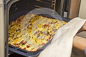 Homemade pepperoni pizza in oven. Delicious pizza cooking in a gas oven. Woman takes a fresh pizza out of the oven