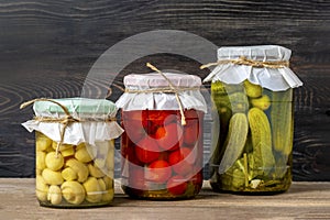 Homemade pickled cherry tomatoes, cucumbers, champignons, garlic, eggplant, red peppers in jars on wooden shelf Homemade canned