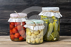 Homemade pickled cherry tomatoes, cucumbers, champignons, garlic, eggplant, red peppers in jars on wooden shelf Homemade canned