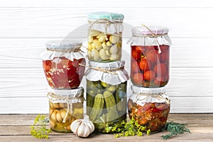 Homemade pickled cherry tomatoes, cucumbers, champignons, garlic, eggplant, red peppers in jars on wooden shelf Homemade canned