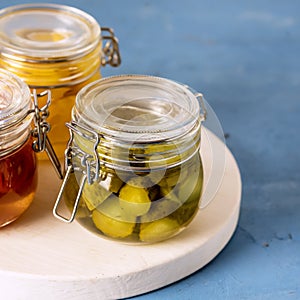 Homemade Pickled or Fermented Vegetables - Pickles, Pickled Tomatoes in Glass Jars Square Blue Background