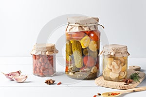 Homemade pickles, pickled mushrooms, canned beans and assorted vegetables in glass jars on a light background