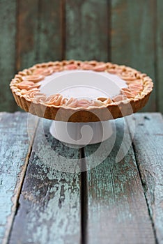 Homemade pie with cream filling and apple roses on stand on wood