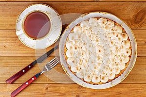 Homemade pie decorated with meringue and a cup of tea on a wooden table.