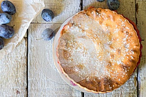 Homemade pie with plums with fork on the white rustic table.