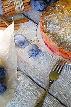 Homemade pie with plums with fork on the white rustic table.