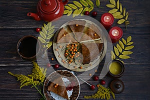 Homemade pie on a wooden plate, red teapot, ceramic mug, candles, sea buckthorn and hawthorn berries, yellow autumn foliage on a