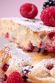 Homemade piece of cake, two pie slices with raspberry and blackberry berries, powdered sugar, in white square plate on pink paper