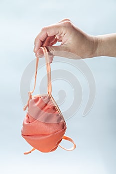 Homemade pink beige fabric mask hanging on the fingers of a female hand on a white background. Vertical orientation