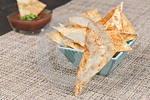 Homemade pita chips in turquoise square bowl on rustic fabric napkin. Red dip sauce in the background. Cooked without oil