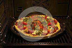 Homemade pizza with fresh tomatoes, mozzarella and arugula in oven, open door, dark background, selective focus, real