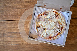 Homemade pizza with mushroom and ham in recycle paper box on wooden table