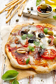 Homemade pizza with tomatoes, olives, salami, mozzarella cheese and fresh basil on a wooden rustic table