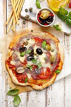 Homemade pizza with tomatoes, olives, salami, mozzarella cheese and fresh basil on a wooden rustic table