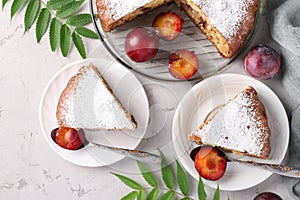 Homemade plum pie sprinkled with powdered sugar cut pieces on plates on light gray background. Top view