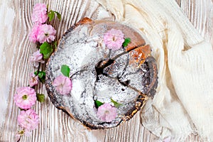 Homemade poppy seed pie with flowers and icing sugar. Yeast round closed cake on a wooden table with a linen tablecloth. Kalach -