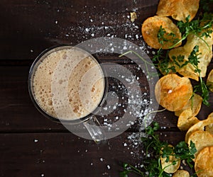 Homemade potato chips with parsley and glass with dark beer on dark rustic wooden table. Tasty fast food. Free copy space for text