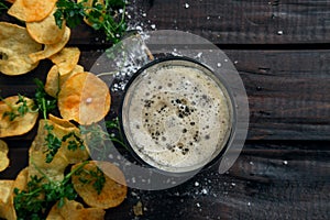 Homemade potato chips with parsley and glass with dark beer on dark rustic wooden table. Tasty fast food. Free copy space for text