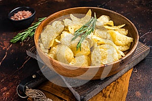 Homemade potato chips with sea salt and rosemary in wooden plate. Dark background. Top view