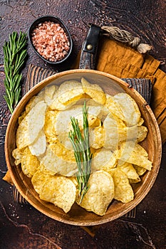 Homemade potato chips with sea salt and rosemary in wooden plate. Dark background. Top view