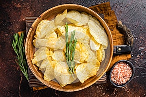 Homemade potato chips with sea salt and rosemary in wooden plate. Dark background. Top view