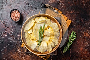 Homemade potato chips with sea salt and rosemary in wooden plate. Dark background. Top view