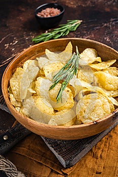 Homemade potato chips with sea salt and rosemary in wooden plate. Dark background. Top view