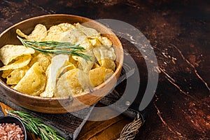 Homemade potato chips with sea salt and rosemary in wooden plate. Dark background. Top view. Copy space