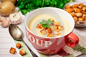 Homemade potato cream soup with croutons and parsley in red bowl on table